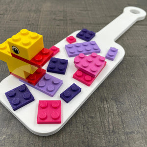 Een kleine BDSM-paddle in de kleur wit met paarse en roze bouwsteentjes