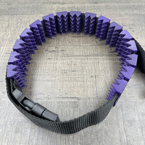 Een BDSM cilice met een zwarte band en spikes in de kleur paars met glitters