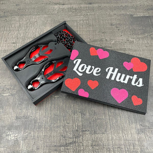 Een set zwarte tepelklemmen in een doosje met de tekst "Love Hurts"