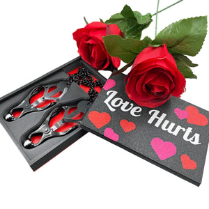 Een set zwarte tepelklemmen in een doosje met de tekst "Love Hurts" en twee rozen