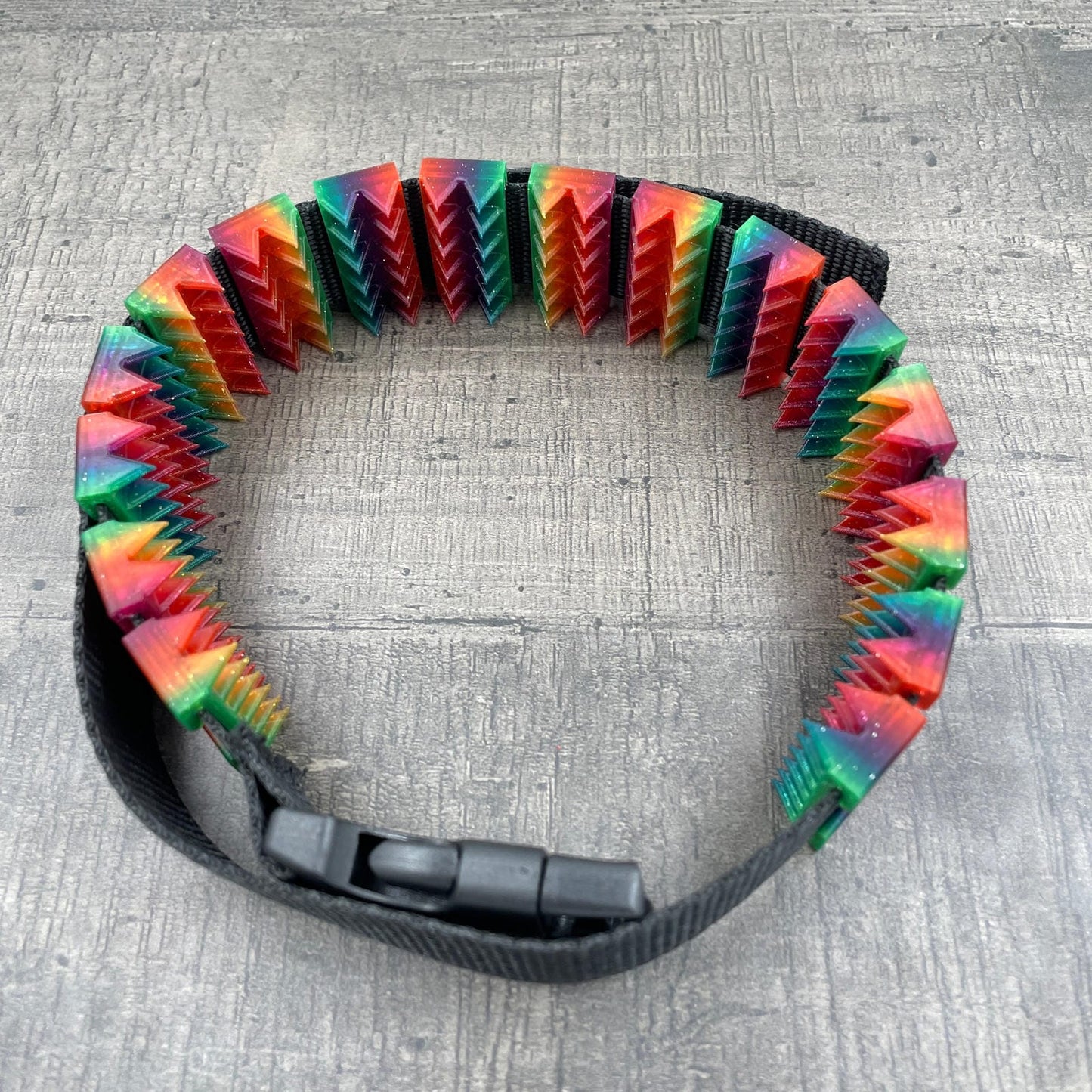 Een BDSM cilice met een zwarte band en spikes in regenboogkleuren met glitters