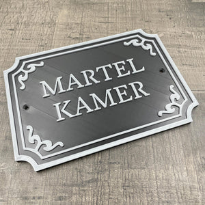 Een zwart deurbordje met de tekst "Martelkamer" in silveren letters.