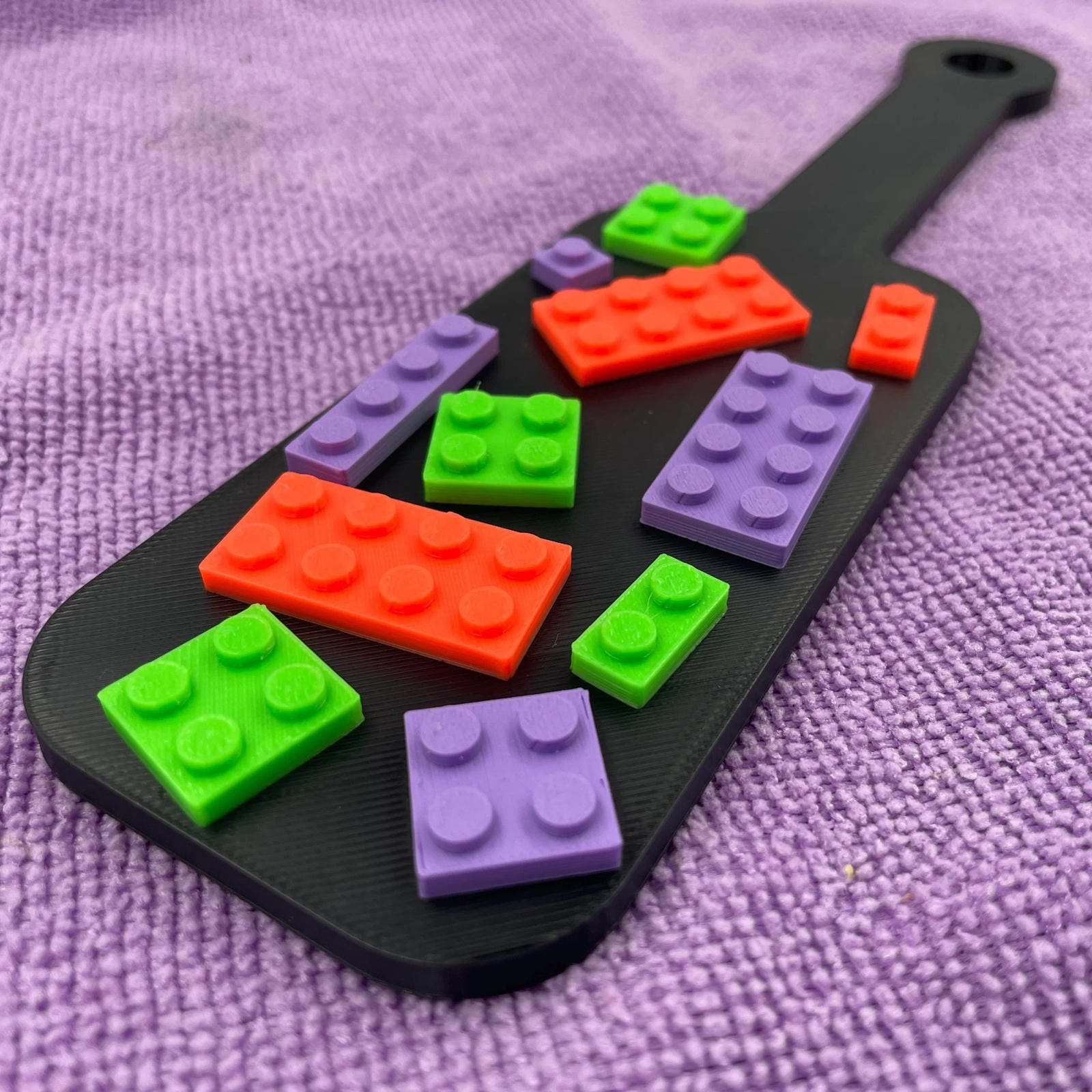 Een kleine BDSM-paddle in de kleur zwart met paarse, oranje en groene bouwsteentjes