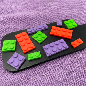 Een kleine BDSM-paddle in de kleur zwart met paarse, oranje en groene bouwsteentjes