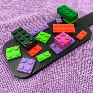 Een kleine BDSM-paddle in de kleur zwart met paarse, oranje en groene bouwsteentjes