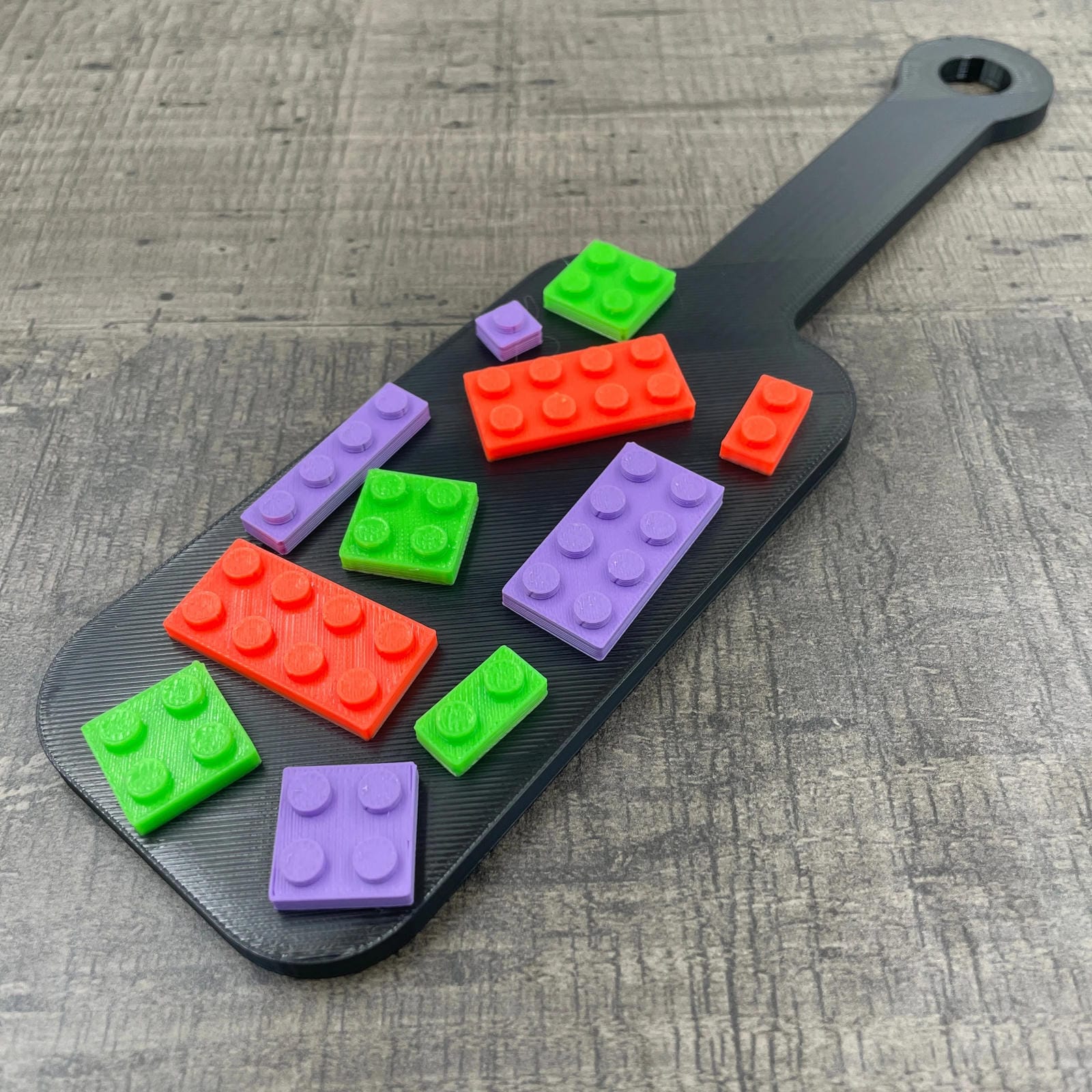 Een kleine BDSM-paddle in de kleur zwart met paarse, oranje en groene bouwsteentjes