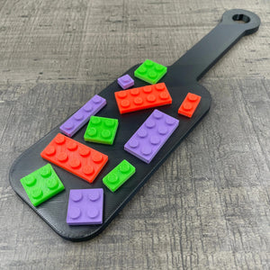 Een kleine BDSM-paddle in de kleur zwart met paarse, oranje en groene bouwsteentjes