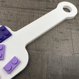 Een kleine BDSM-paddle in de kleur wit met paarse en roze bouwsteentjes