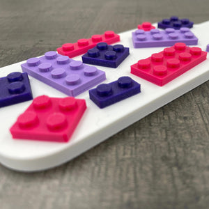 Een kleine BDSM-paddle in de kleur wit met paarse en roze bouwsteentjes