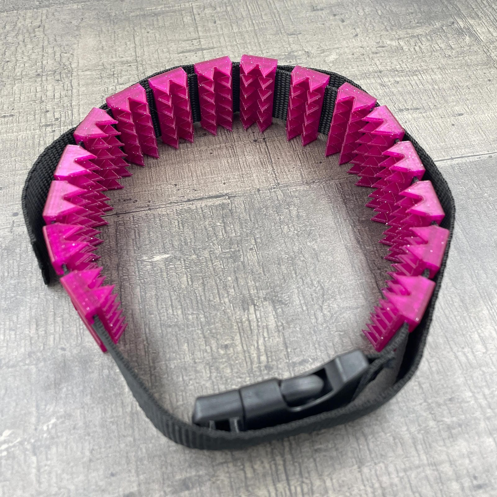 Een BDSM cilice met een zwarte band en spikes in de kleur magenta met glitters
