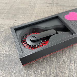 Een zwarte BDSM Wartenberg pinwheel in een doosje met de tekst "Love Hurts"