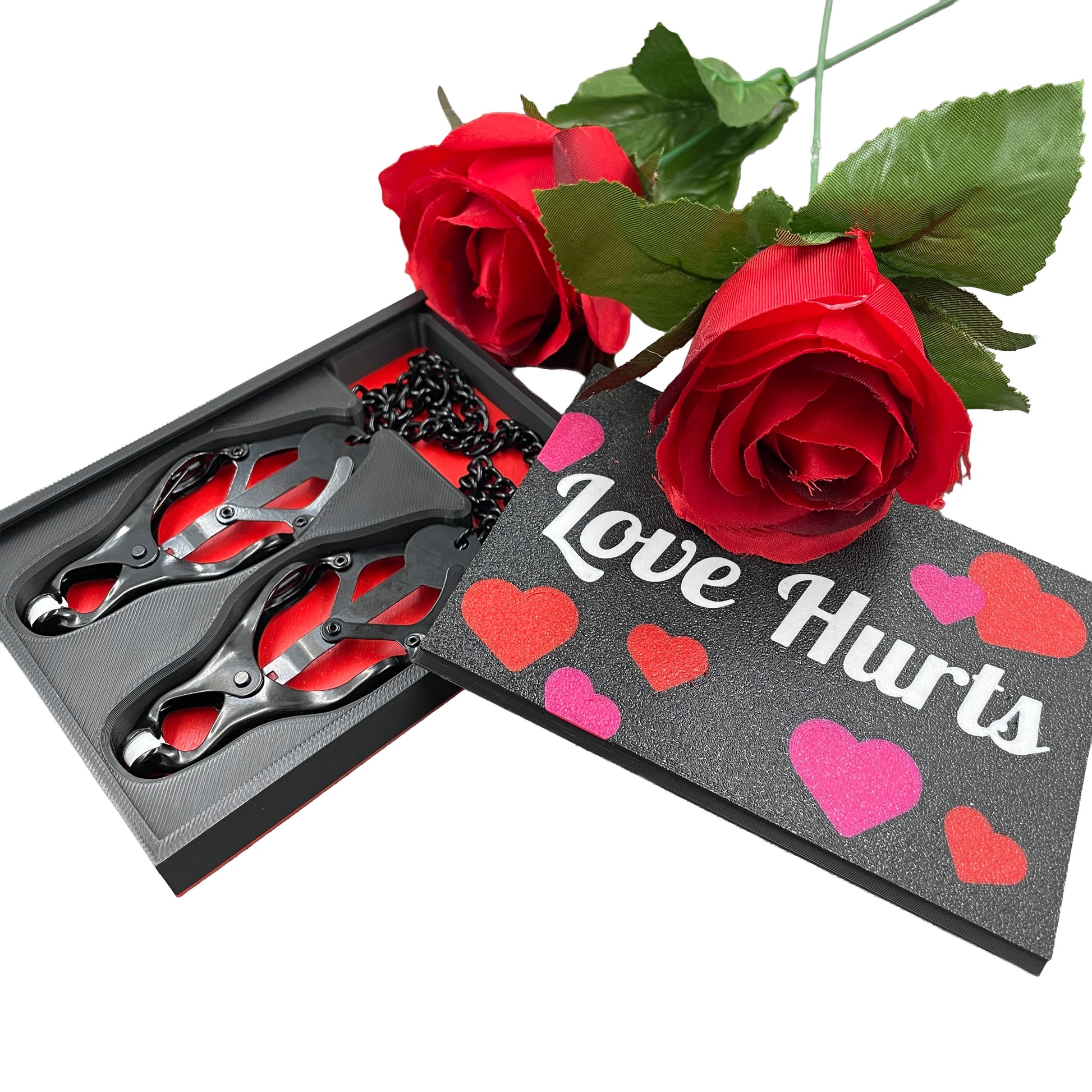 Een set zwarte tepelklemmen in een doosje met de tekst "Love Hurts" en twee rozen