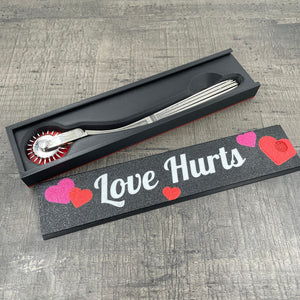 Een silverkleurige BDSM Wartenberg pinwheel in een doosje met de tekst "Love Hurts"
