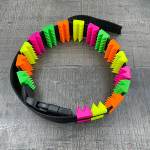 Een BDSM cilice met een zwarte band en spikes in UV-reactieve kleuren