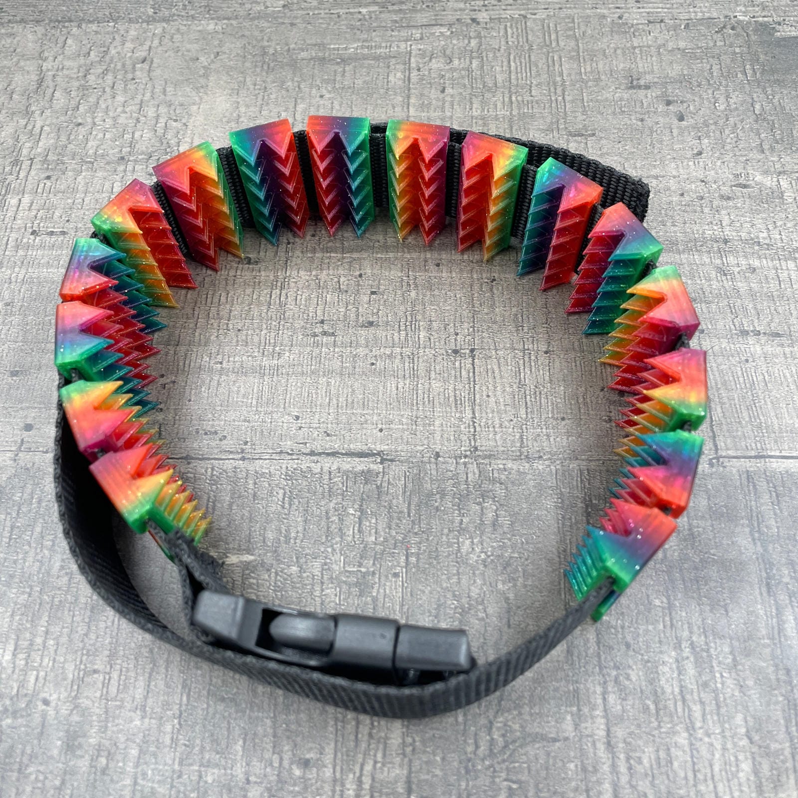 Een BDSM cilice met een zwarte band en spikes in regenboogkleuren met glitters