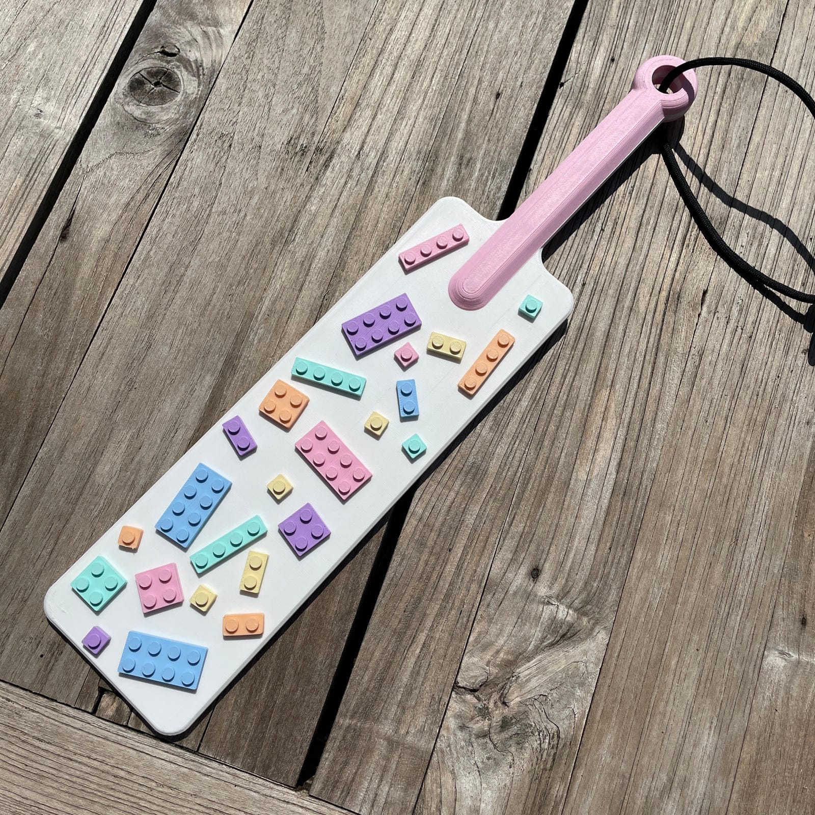 Een BDSM paddle in wit met pastel-kleurige bouwsteentjes en een roze handvat