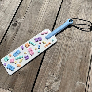 Een BDSM paddle in wit met pastel-kleurige bouwsteentjes en een blauw handvat