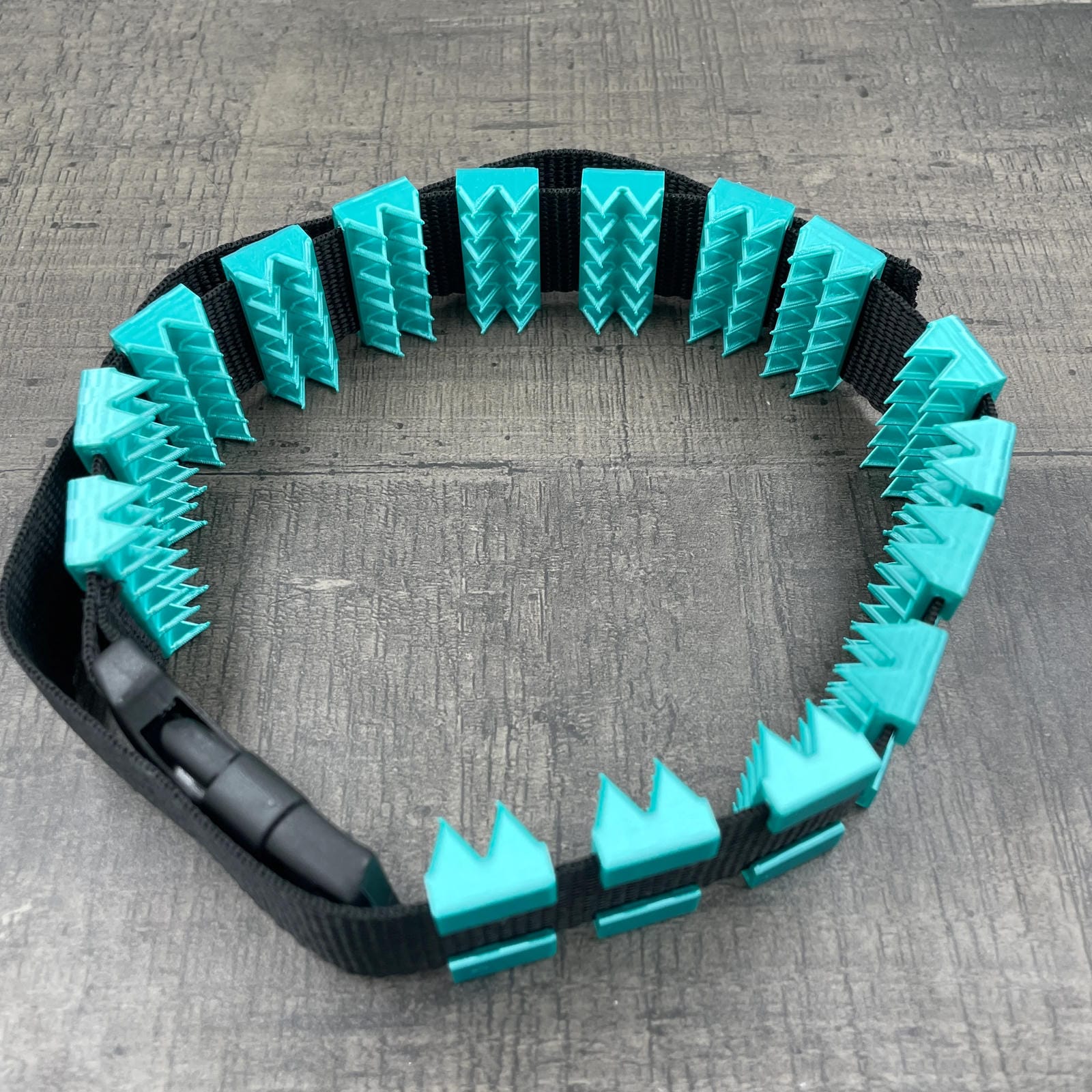 Een BDSM cilice met een zwarte band en spikes in turquoise